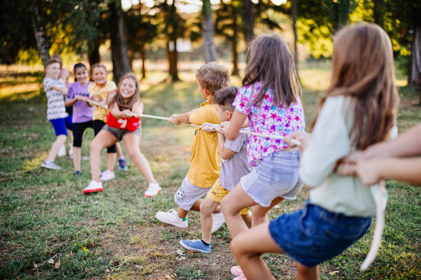 Large group of playful kids having fun in the park while playing tug-of-war.
